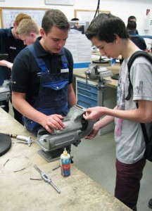 Ein Auszubildender hilft einem jungen Besucher bei der Anfertigung des Werkstückes.