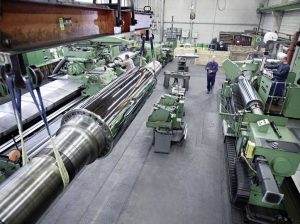 Ein Blick in die Schleifhalle. Vorne hängt eine Kalanderwalze am Kran. Sie verfügt über periphere Bohrungen und über eine verchromte und polierte Ballenoberfläche.